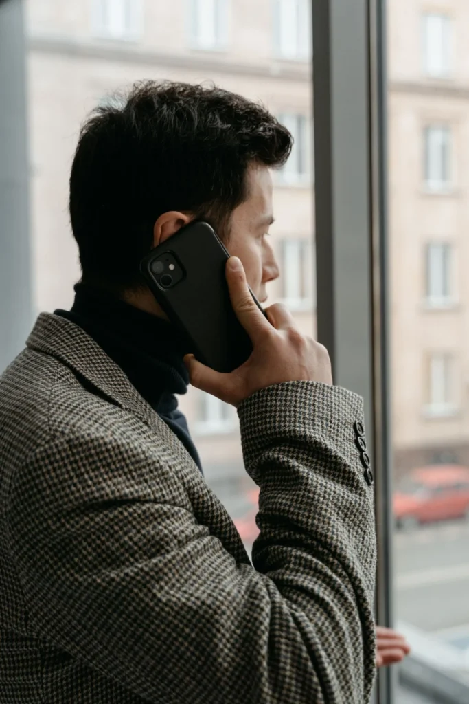 Mann i blazer bruker mobilen ved vinduet