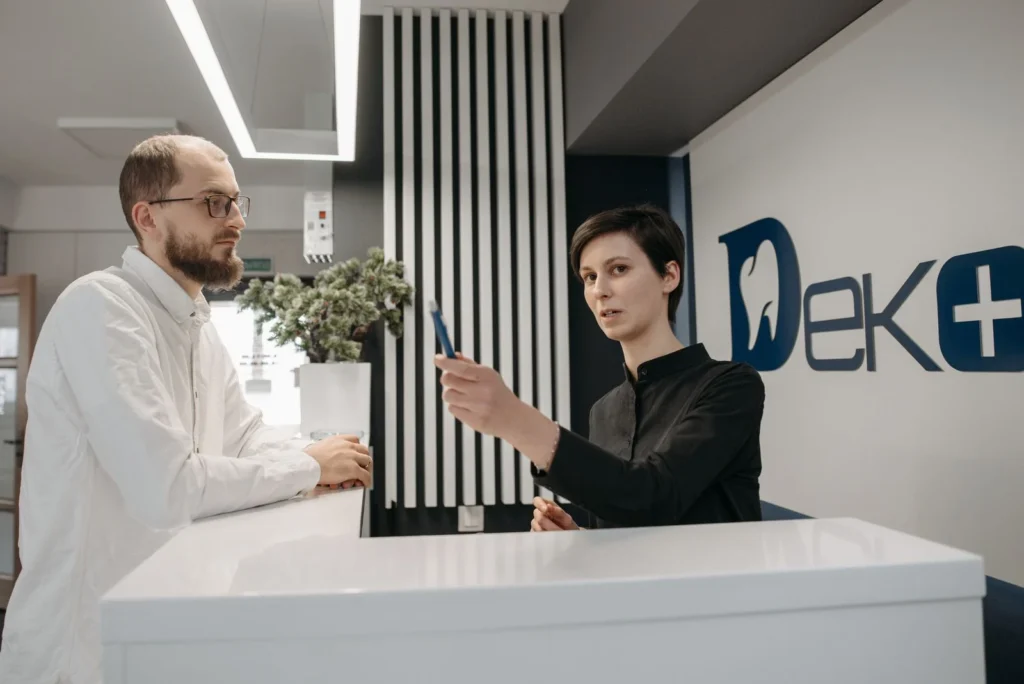 Resepsjonist ved skranken på et legekontor i samtale med en pasient